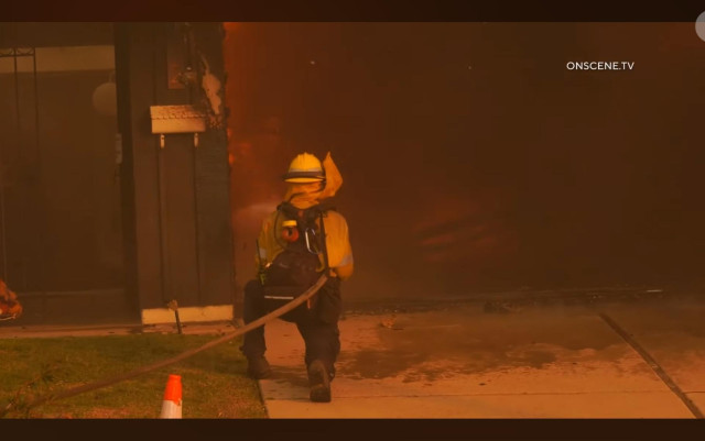 Fire fighter pointing hose at burning house