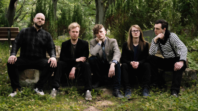 The band Soulsplitter is sitting on a bench in front of trees.