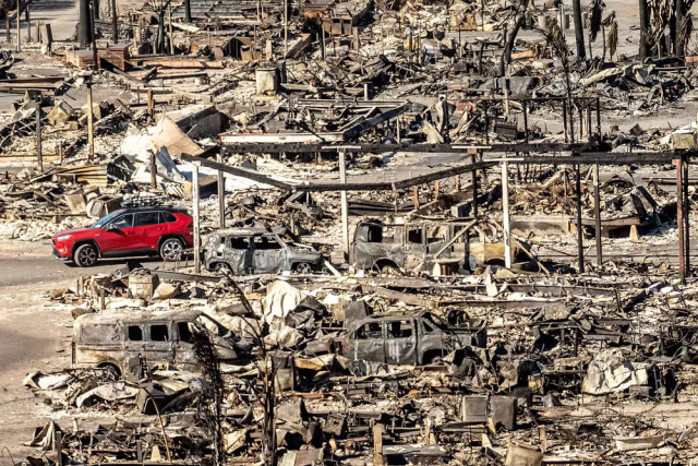 Un SUV rouge roule parmi les rue et les voitures incendiées de Los Angeles