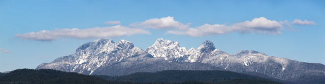 Panorama of 3 mountain peaks (The Golden Ears) on a slue sky day with a ribbon of clouds over top of the peaks