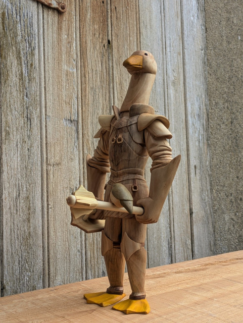 Woodcarved humanoid goose wearing an armour plate, holding a shield and a mace with a red robin on the handle