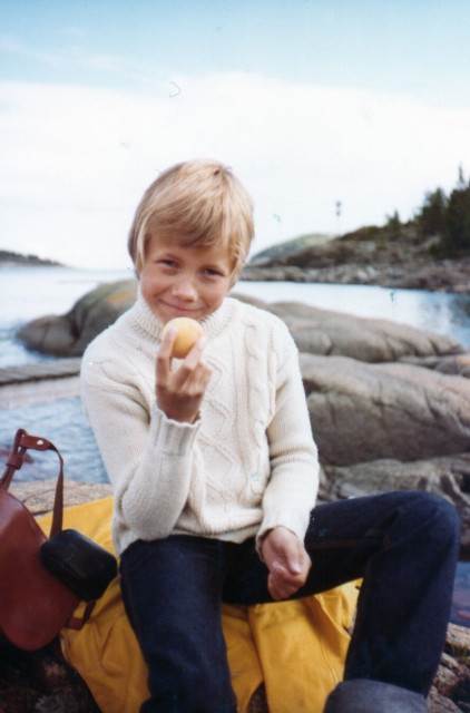 Photo of a pre-teen boy (me) sitting on a rock by a lake.