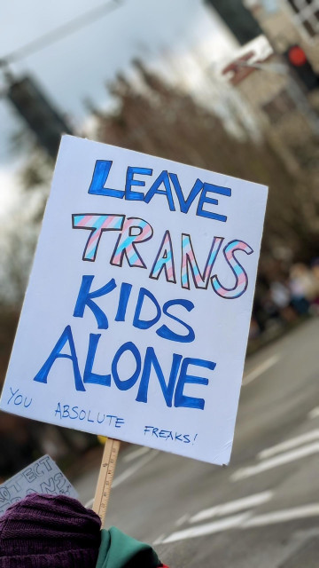 A protester's sign that reads "Leave trans kids alone" in large blue and pink lettering, with smaller text below that says "You absolute freaks!".