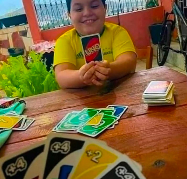 Two people playing Uno. POV of a player holding four cards three of them are +4 and one is +2. Facing a young, smiling child, clearly holding one card and think they will win.