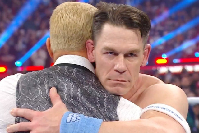 John Cena hugging Cody Rhodes while staring behind Cody at the Rock with an evil face.