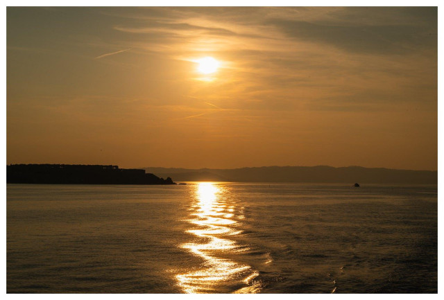 Bild in den Sonnenuntergang, links eine Halbinsel, rechts in kleines Motorboot.