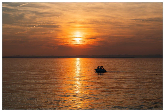 Bild in den Sonnenuntergang und ein kleines Motorboot als Silhouette.