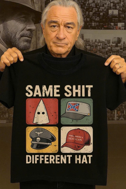 An older man holds a black t-shirt featuring a graphic design with four different hats and the text "SAME SHIT DIFFERENT HAT." The hats depicted include symbols associated with various controversial groups and movements. 
Robert de Niro.