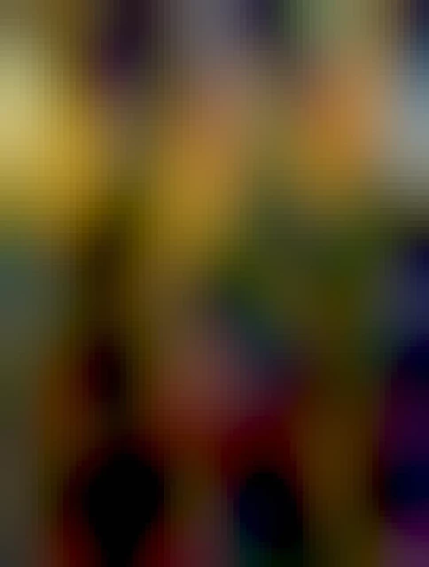 Large trees bright with autumn colours are seen in the woods. A path covered in orange leaves makes its way through the forest. Blue sky can be seen in the top right of the picture.