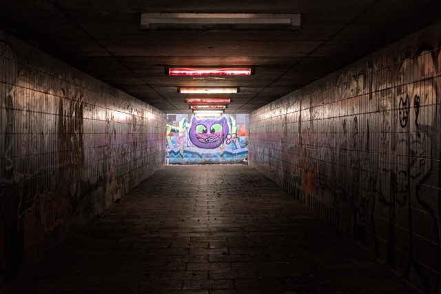 Tunnel mit Graffiti an den Wänden, am Ende eine bunte Darstellung der Grinsekatze aus Alice im Wunderland.