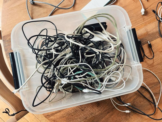 an overhead photo showing a clear plastic box sitting on a wooden table... which contains a large number of cables, all tangled up