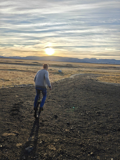 A man unicycling towards the sunrise along a gravel path. 