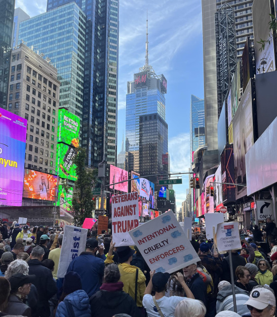 Many people in Times Square. Some are holding protest signs. People are chatting and waiting patiently. 
