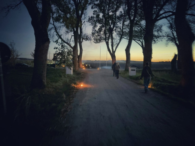 A country road in the night, with lanterns leading to a Halloween labyrinth in a corn field.