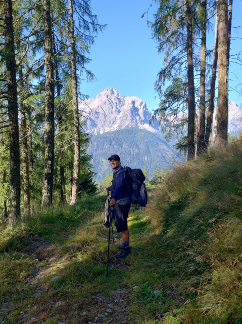 I stand in the middle of a forest path and smile - a bit forced - into the camera. The Sexten Dolomites rise in the back.