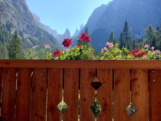 A wooden, flower-adorned balcony at Talschlusshütte. The Sexten Dolomites rise in the back. The sky is light blue.