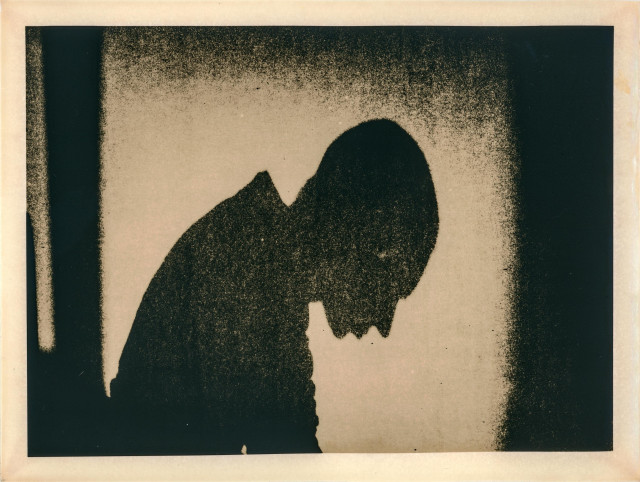 This lith print portrays a solitary human figure in profile, head slightly bowed, rendered in stark contrast and heavy grain. The coarse texture and deep blacks create an atmosphere of introspection and melancholy. The background fades into a hazy light, enhancing the sense of isolation and giving the image a ghostly, almost spiritual quality. The print’s tonal shifts — from velvety black to warm beige — evoke both fragility and permanence, as if the figure is dissolving into light or memory.