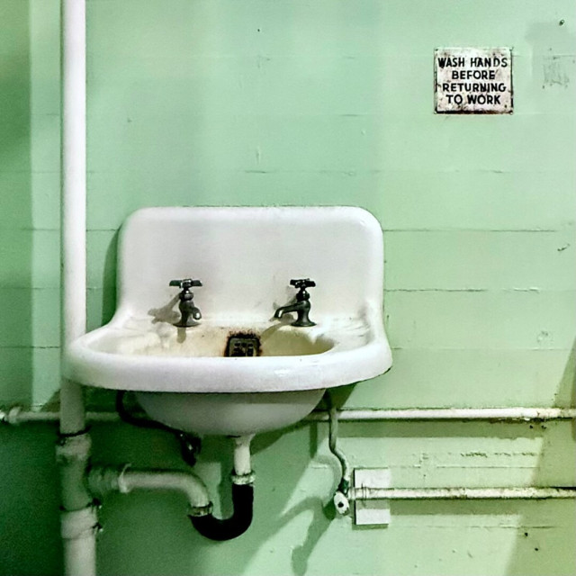 Dirty white sink against a mint green wall with a sign that says "wash hands before returning to work"