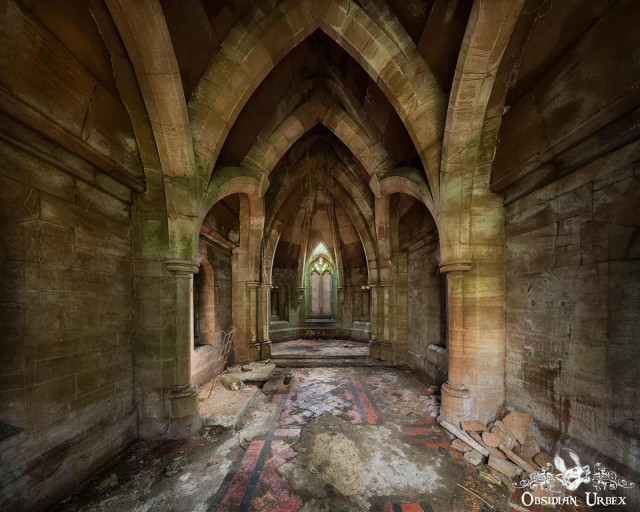 The interior of an abandoned or ruined gothic crypt or church with stone columns, vaulted ceilings, and a dirty floor with red and black tiles