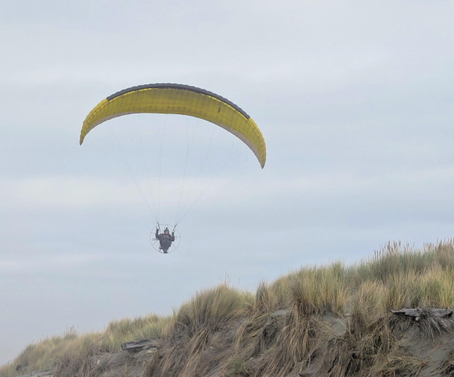 A yellow hang glider is flying low over the beach.