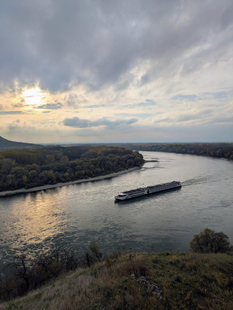 Blick auf die Donau Richtung Österreich bei Sonnenuntergang. Ein Flusskreuzfahrtsschiff verkehrt flussabwärts.