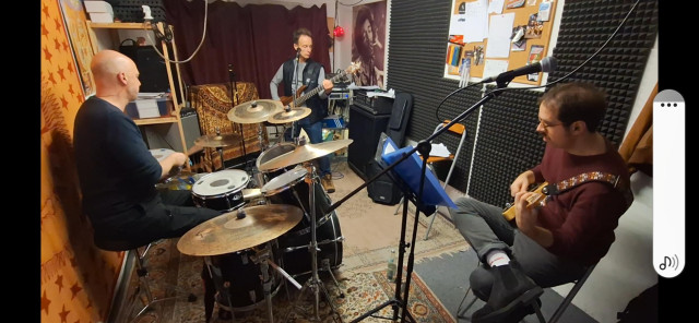 Fish-eye view of rehearsal space with the band. Drums, guitar, bass. All dressed casually