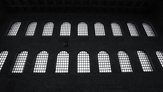 18 identical, arched windows in a double row, set into a dark wall.