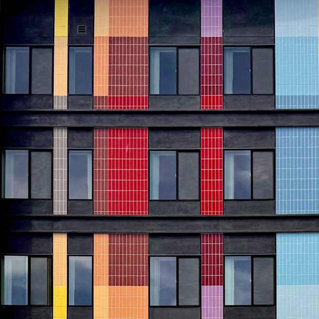 Facade of an apartment building or hotel with brightly colored tall vertical tile accents in a variety of rainbow colors except greens.
