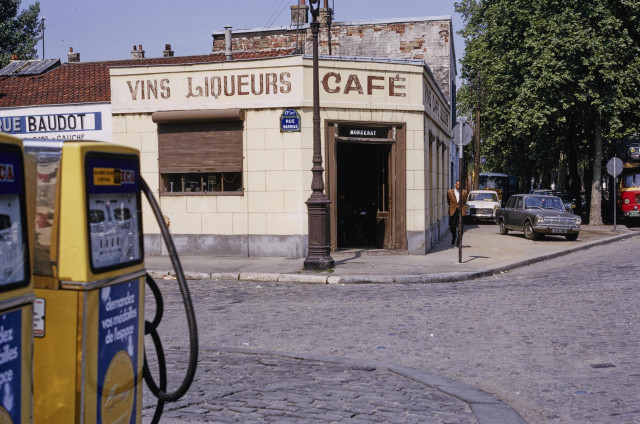 Un bâtiment avec une enseigne "vins liqueurs café" et une pompe à essence au premier plan