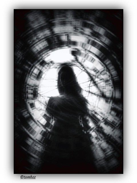 Black and white photo with a cool tone. The woman is shot from below and her figure is blurred, wrapped in a glitchy ring that looks like a digital ripple. You can't see her face, just the outline of her long hair and dress. The background is wild twisted city shapes stretched into a spinning circle, like the whole scene got sucked into a vortex. It feels dreamy and a bit unsettling, like a memory glitch caught between emotion and static.