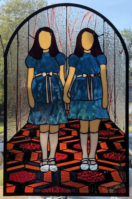Stained glass panel of the Grady Sisters from The Shining, standing on the iconic orange and red patterned carpet. The background is clear glass with red streaks, as if from blood.