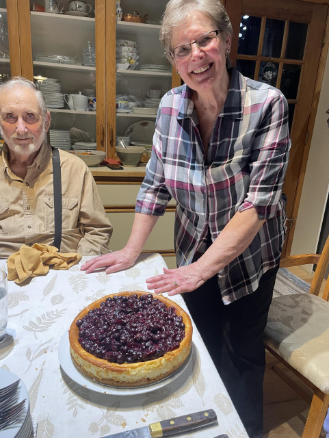 My mom smiles as I take a picture of her creation. My step dad smiles sitting at the end of the table in front of a glass china cabinet 
