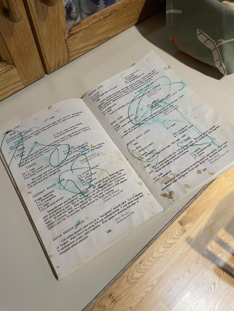 The book opens to reveal pages with green crayon doodles scrawled across