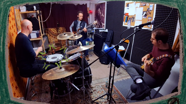 Screenshot of a video. A band in a reheasal room, framed in a crayon-painted TV. Motion lines on the drumhead indicate sound.