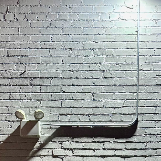 Brick wall and an exterior lighting system with power line that have all been painted over in white. It's nighttime and the wall is illuminated from another source as the other exterior lights in the photo aren't on.
