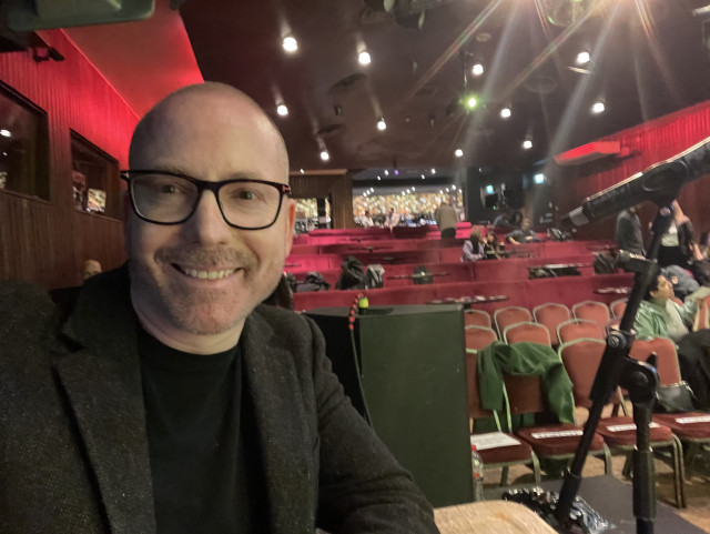 Yours truly smiling into the camera with a speakeasy style venue in the background.
