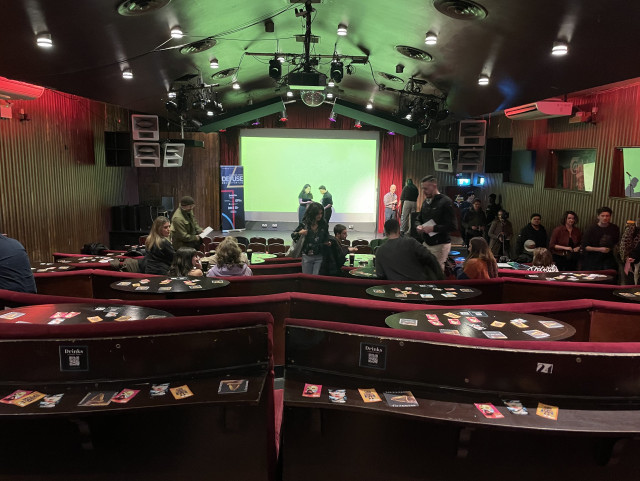 Photo of the venue showing the red speakeasy style seating and the stage with a projector screen.