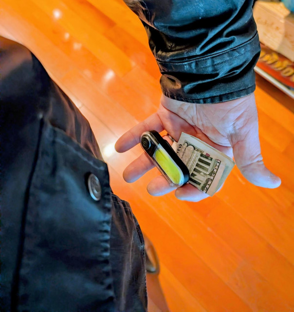 Downward-shot photo of my coat pocket, LED safety light and a $5 bill