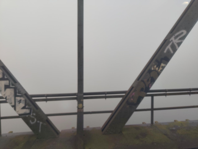 A shot out a train, looking out over a railway bridge fence. Beyond, there is only fog visible.