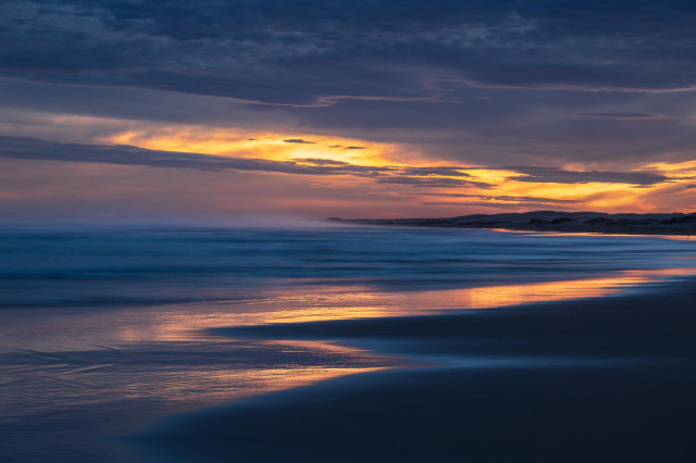 sunset beach with the slowly receding water reflecting sunset colours and orange sunset sky with heavier clouds at the top