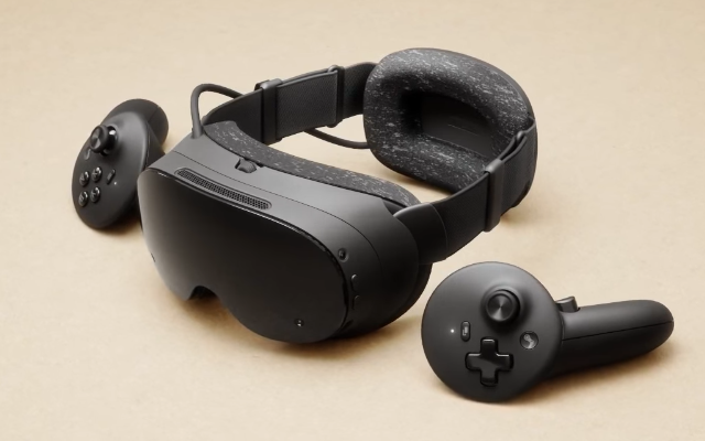 But this is. A cool looking set of black VR goggles with two futuristic looking controllers lay on a beige surface.