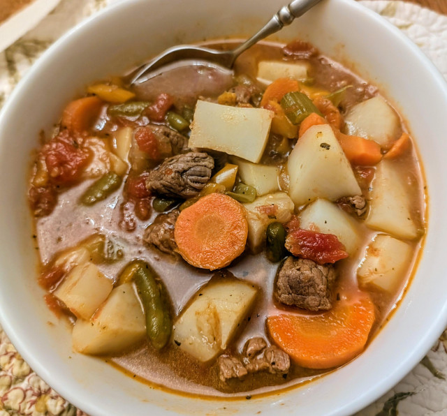 A white bowl full of vegetable beef soup.