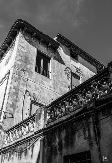 Black and white photo looking up at the corner of an old building with a decorative stone railing.