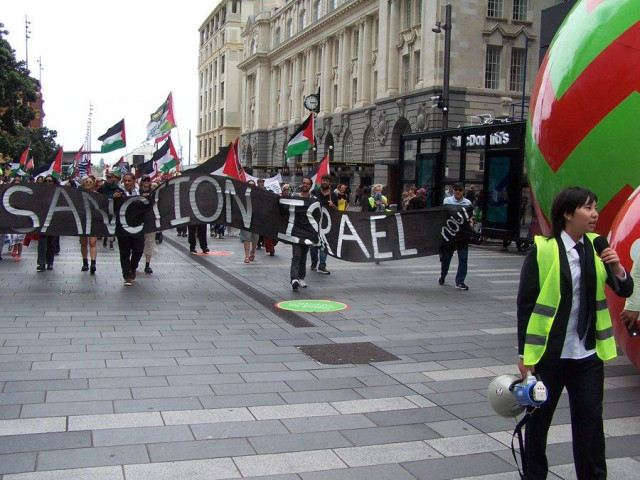 Crowds with flags and placards marching through Auckland behind a banner reading SANCTION ISRAEL NOW