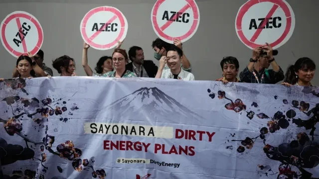 Protesters hold a massive banner with cherry blossoms and a greywash image of Mount Fuji, along with the slogan SAYONARA DIRTY ENERGY PLANS.