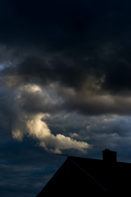 A curve of cloud catches sunlight in a glowering sky, like smoke rising from the dark chimney below.