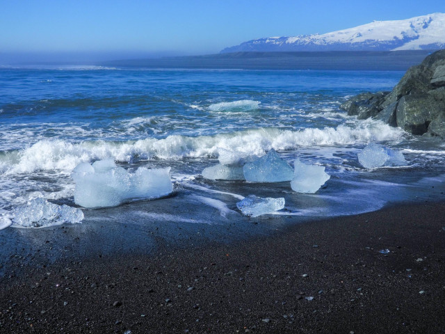 Small chunks of iceberg washed ashore by waves on a black sand beach.