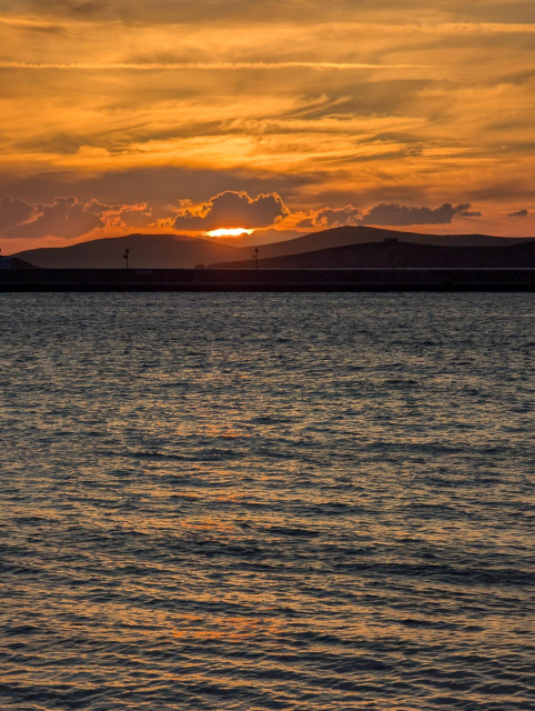 A deep orange sunset peaking through dark terrain, Mykonos