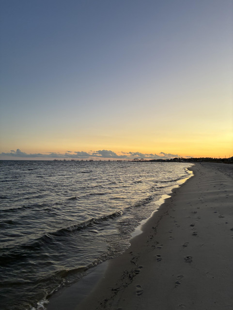 Coast view with sun setting yellow and white-trimmed surf hitting the beige beach. 