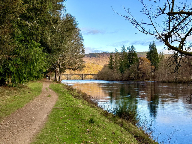 Two lovers strolling by the Tay River during autumn — Dunkeld bridge, yellow-orange trees in the background 